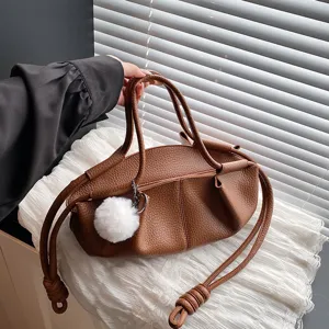 Brown soft leather cloud bag detail showing stylish slouchy design and cute plush pom-pom pendant.