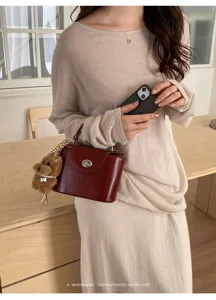 Detail view of structured dark red handbag with turn-lock clasp and cute plush dog charm.