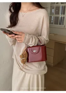 Detailed view of the elegant structured box handbag with twist lock and cute plush charm.