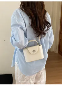 Elegant white structured box handbag with turn lock detail worn by model in casual outfit.