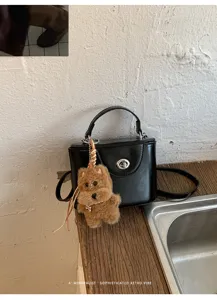 Close-up detail of trendy black box handbag featuring cute plush animal keychain charm.