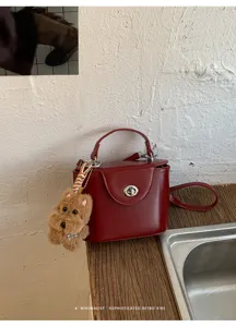 Detailed view of a trendy dark red retro box handbag with turn-lock and cute dog charm.