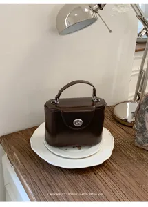 Retro dark brown box handbag detail view on white ceramic plate with stylish vintage table lamp.