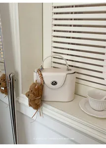 Close-up detail of cream retro box handbag with cute fluffy teddy charm on windowsill.