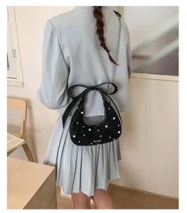 Close-up detail of stylish black quilted shoulder bag featuring elegant pearl and bow.