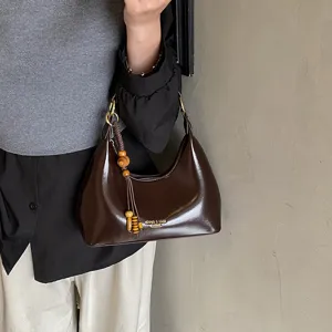 Brown patent leather hobo shoulder bag detail, elegant casual handbag with beaded tassel charm.