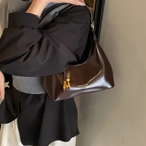 Brown leather underarm hobo bag with wooden bead pendant and metal zipper detail style.