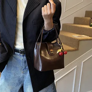 Detailed view of women's retro bucket handbag featuring a cute cherry charm and metal lock.