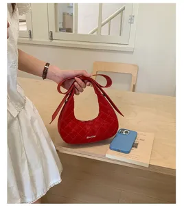 Close-up of red quilted crescent handbag with bow handle in a bright minimalist room setting.