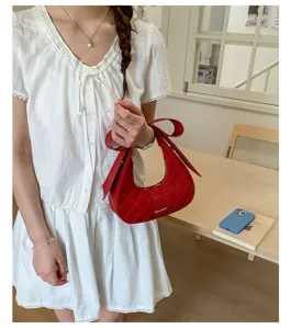 Detailed shot of a red quilted crescent shoulder bag with elegant bow detail on woman.