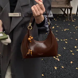 Detailed view of women patent leather hobo bag with wooden bead charm and shoulder strap.
