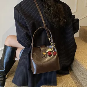 Vintage dark brown leather bucket bag detail with golden clasp and cute cherry charm.