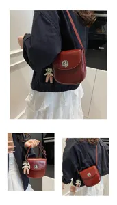 Detail view of stylish dark red crossbody phone bag with cute doll pendant and metal lock.