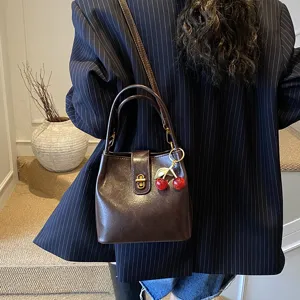 Detail shot of a chic dark brown leather bucket bag with a cute cherry charm for women