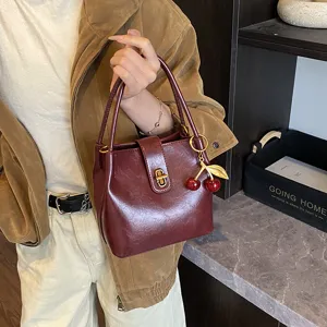 Burgundy bucket bag detail shot, featuring retro metal lock and cute cherry charm.