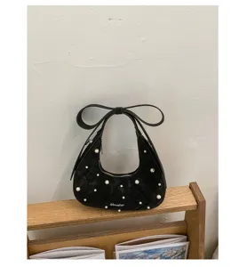 Detail view of black quilted women shoulder bag with elegant pearl embellishments and bow handle.