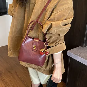 Stylish burgundy bucket bag featuring a chic gold turn-lock closure and playful cherry charm.