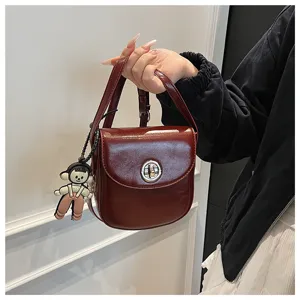 Detailed view of the stylish burgundy leather crossbody bag with cute doll charm and metal lock.