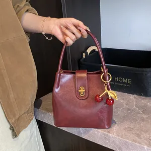 Detail shot of retro wine red bucket bag with cherry charm, elegant handheld design style.