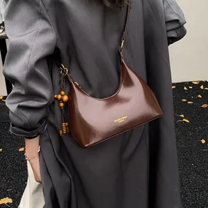 Detailed shot of brown patent leather underarm shoulder bag with vintage beaded charm decor.