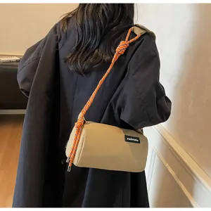 Detail shot of khaki cylindrical crossbody bag with vibrant orange rope strap and front label.