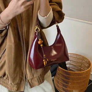 Close-up of wine red patent leather underarm hobo bag detail with wooden bead charm.
