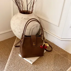 Detailed view of women's brown bucket bag featuring gold-tone hardware and cute cherry charm pendant.