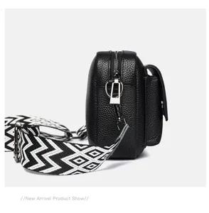 Detalle de bolso cruzado de cuero negro con textura, herrajes plateados y correa estampada.