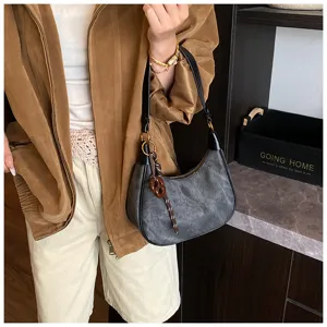 Primo piano di una borsa a tracolla vintage grigio scuro opaco con elegante ciondolo in metallo.