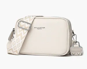 Detailed view of white leather crossbody bag with wide strap, high quality hardware and zipper.