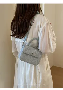 Primer plano del bolso cruzado tejido azul claro con cerradura metálica y estilo retro.