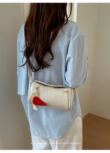 Borsa a tracolla cilindrica bianca minimalista con ciondolo a carota rossa dettaglio.