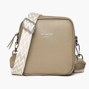 Detailed view of women khaki leather crossbody bag, featuring wide patterned strap and metal hardware.
