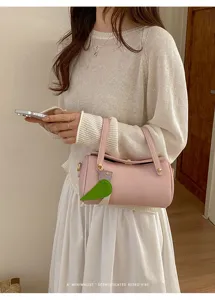 Dettaglio di borsa a spalla cilindrica rosa minimalista con elegante ciondolo floreale.