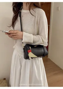 Vista dettagliata della borsa a spalla cilindrica nera con ciondolo a uccello stile rétro.