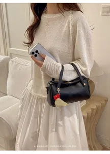 Vista dettagliata di una borsa a spalla cilindrica nera minimalista con grazioso ciondolo a uccello.