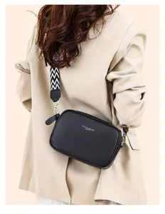 Detailed view of the black leather crossbody bag featuring wide geometric strap and metal hardware.