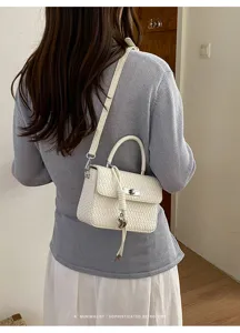 Vista detallada del elegante bolso cruzado tejido en blanco con asa superior y cierre de giro.