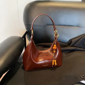 Detailed view of retro brown leather underarm bag with zipper and wooden bead charm pendant.