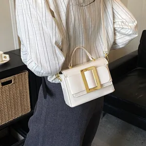 Detail shot of white patent leather shoulder bag with gold metal buckle and top handle.