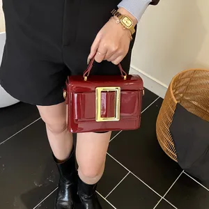 Detail view of a retro wine red patent leather handbag with gold buckle and stylish shoulder strap.