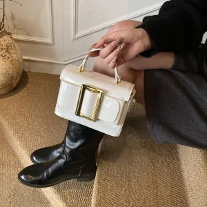 Detail shot of white patent leather shoulder bag with gold metal buckle, stylish daily look.