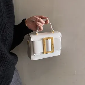 White patent leather handbag with bold gold buckle, stylish vintage shoulder bag.
