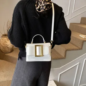 Close-up of a stylish white patent leather shoulder bag with bold gold-tone buckle detail.
