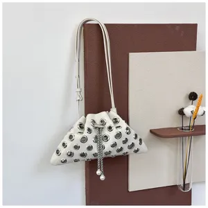 Detail view of white leather shoulder bag featuring metallic grommets and pearl drawstring.