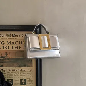 Detail shot of vintage metallic silver shoulder bag with oversized gold square buckle.