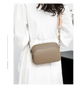 Close-up detail of women's leather crossbody bag with patterned strap and metal zipper.