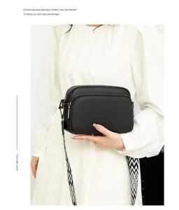 Detailed shot of black pebbled leather crossbody bag, compact square design with chic strap.
