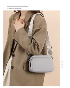 Grey pebbled leather crossbody bag detail featuring a stylish woven wide strap and sleek zipper.
