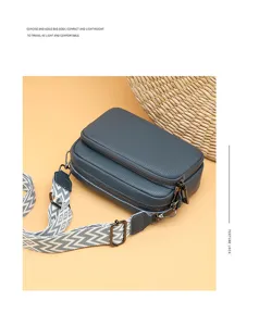 Detail shot of the dark blue pebble leather cross-body bag with dual zippers and strap.